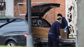 Trabajadores de una funeraria introducen un ataúd en un coche fúnebre.