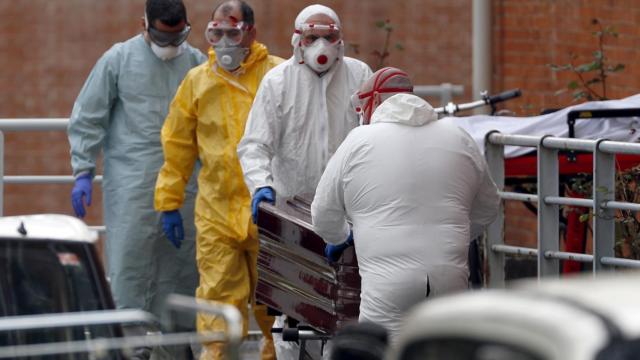 Trabajadores de una funeraria protegidos trasladan de la morgue a un fallecido por coronavirus.