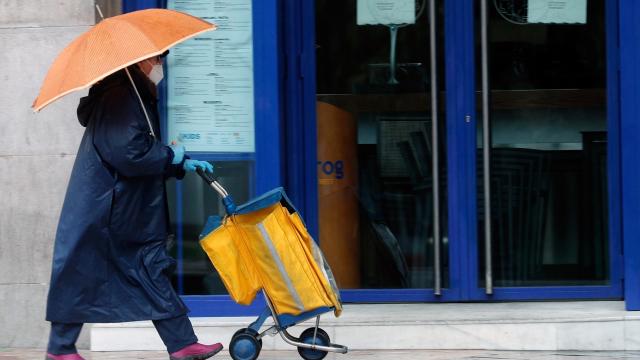 Una cartera, protegida con mascarilla, reparte el correo bajo la lluvia.