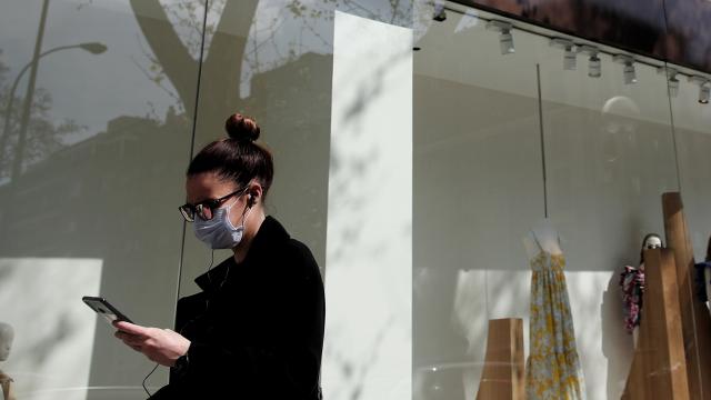 Una mujer con mascarilla maneja un móvil frente a una tienda.