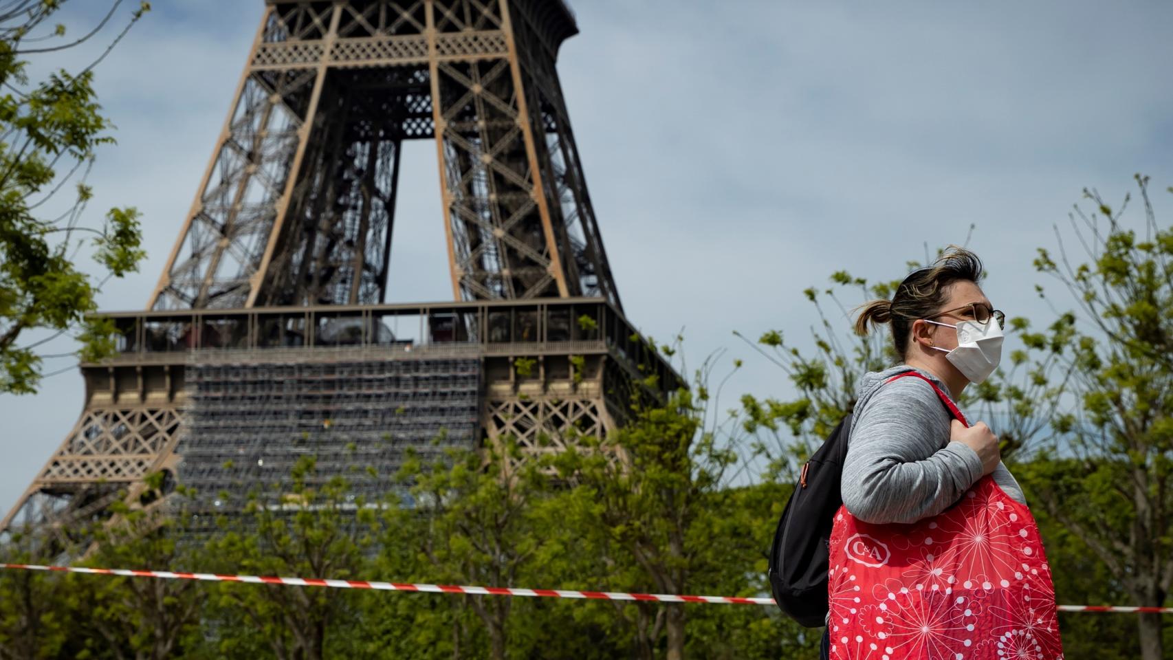 Una mujer camina con mascarilla cerca de la torre Eiffel