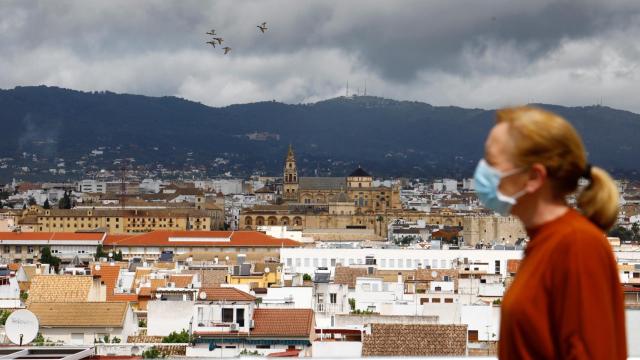 Una mujer camina por Córdoba. Al fondo la Mezquita-Catedral y el cielo cubierto de nubes oscuras.