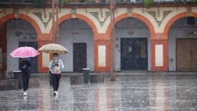 Dos mujeres protegidas con mascarillas y paraguas caminan por Córdoba. EFE/Salas