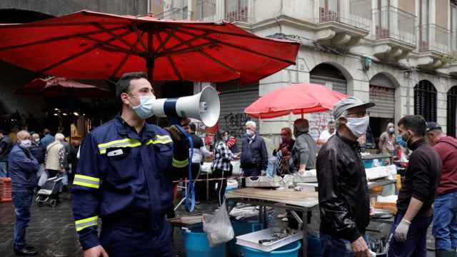 Un voluntario de protección civil pide, a través de un megáfono, mantener la distancia de seguridad en un mercado de Catania.