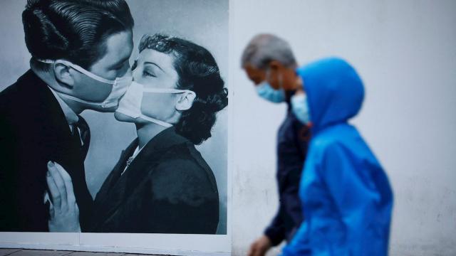 Personas protegidas con mascarilla pasan junto a un dibujo de un beso con mascarillas en Córdoba. EFE/Salas.