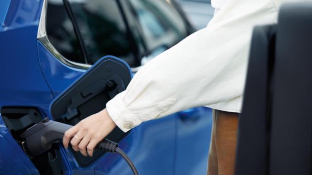 Una mujer cargando un vehículo eléctrico.