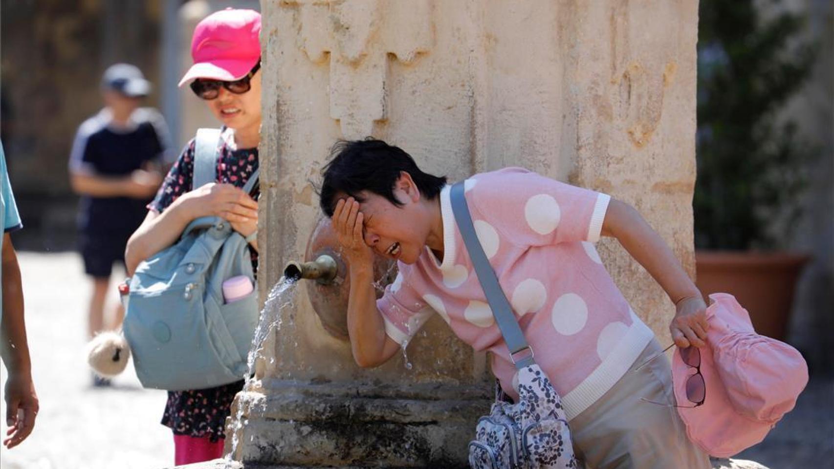 Turistas extranjeros se refrescan en una fuente en Sevilla.