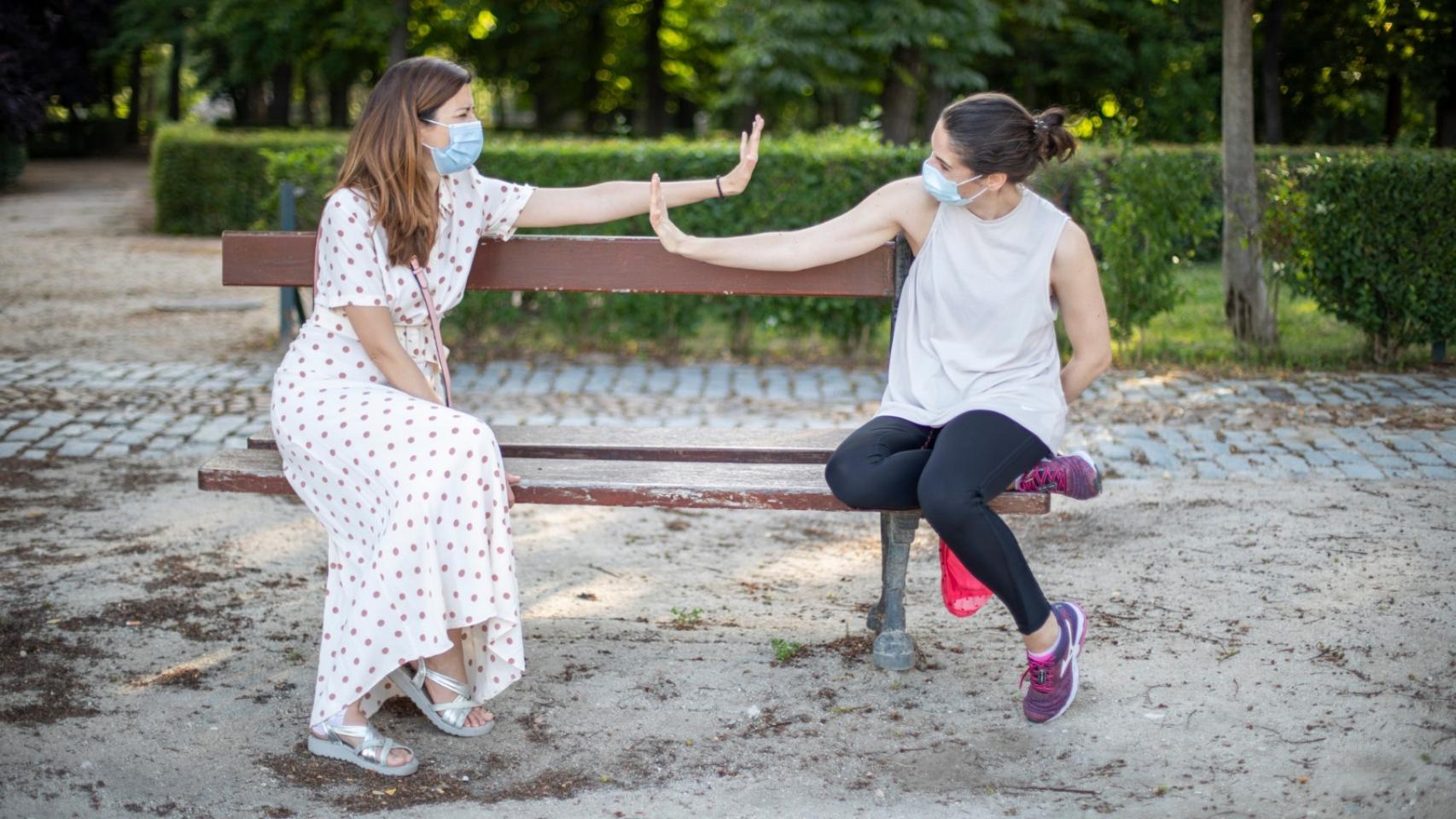 Dos amigas simulan saludarse sentadas en un banco del céntrico parque madrileño.