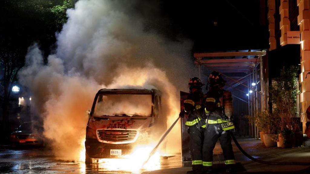 Los servicios de emergencias apaciguan un coche incendiado por los manifestantes.
