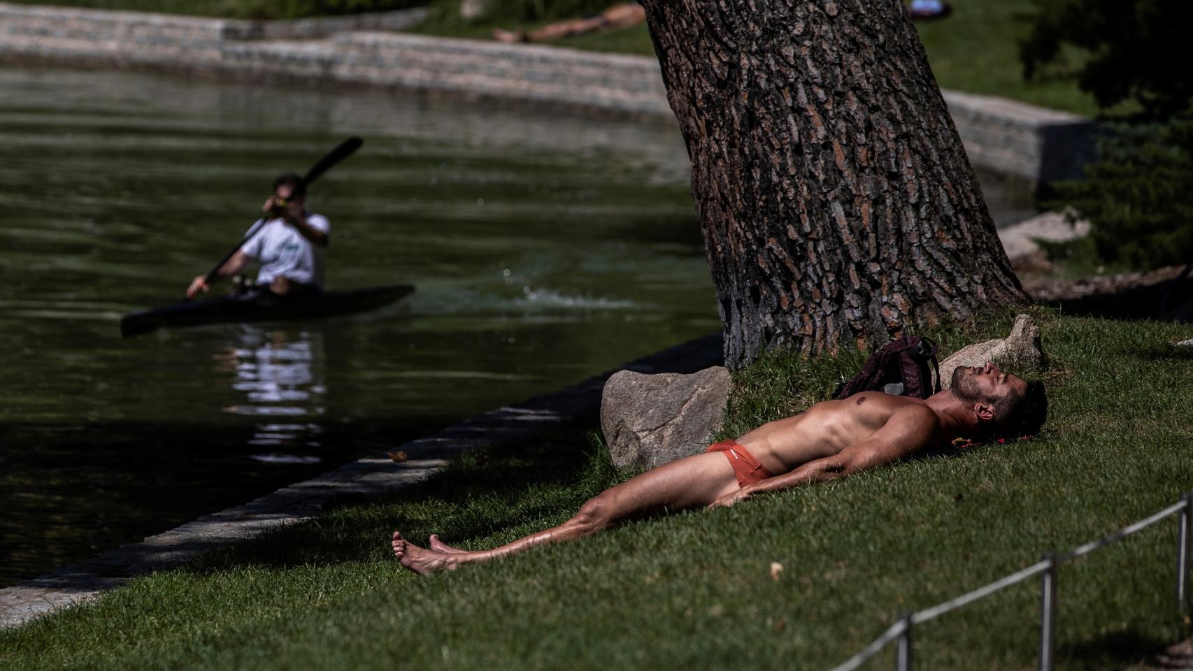 Un hombre hace deporte en una piragua mientras otro toma el sol en el lago de la Casa de Campo en Madrid este martes.