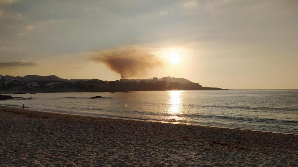 El humo saliendo del incendio en O Portiño visto desde la playa del Orzán.