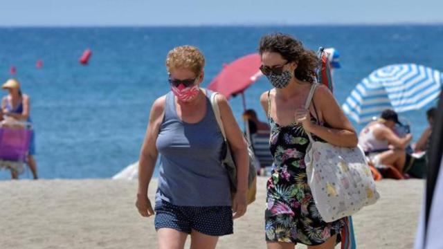 Un hombre y una mujer paseando en la playa con mascarilla.