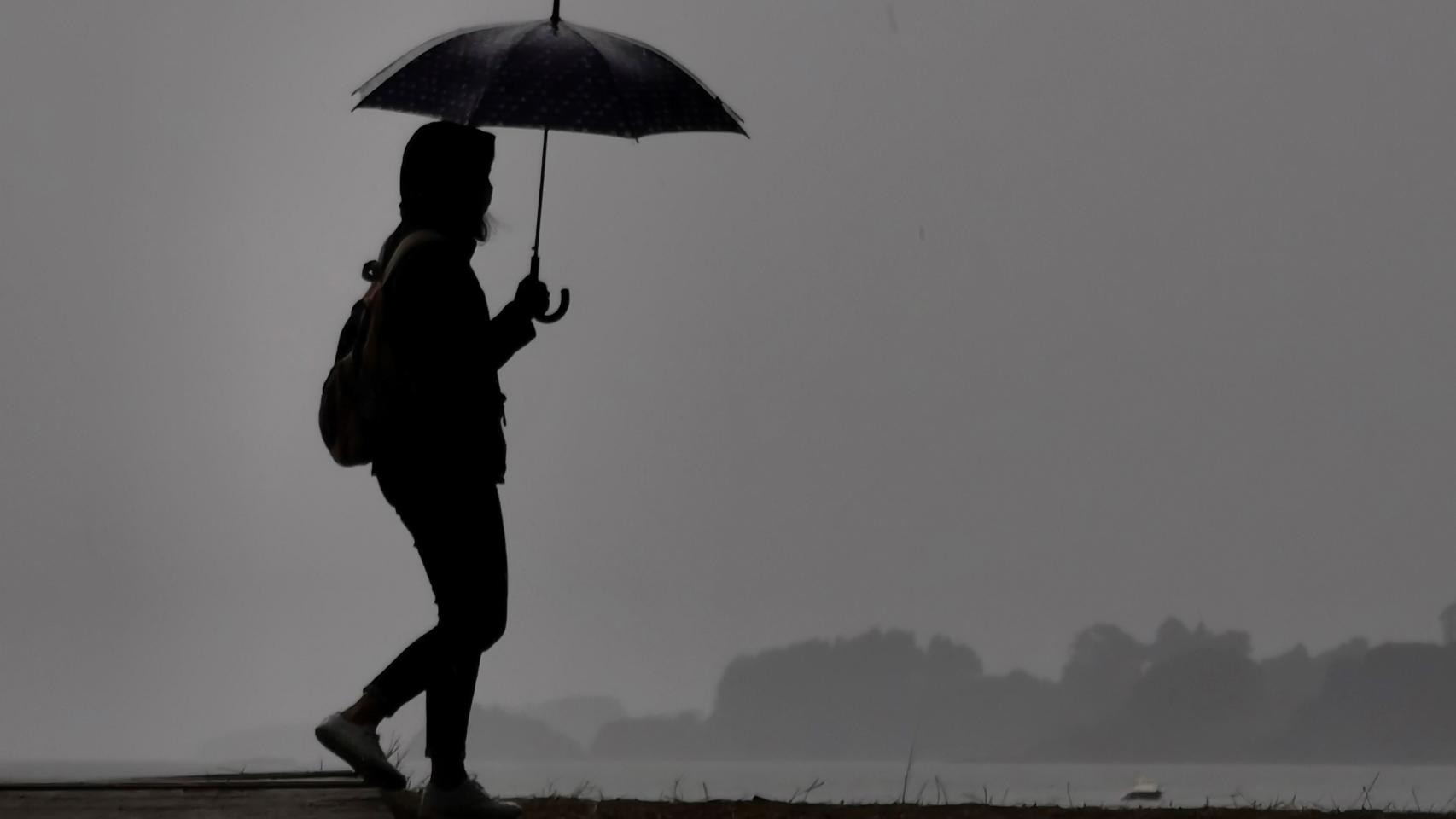 Una mujer pasea bajo la lluvia en Galicia.