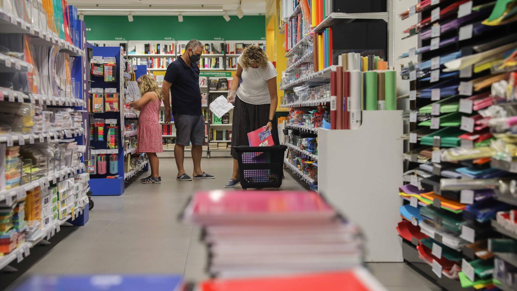 Una pareja acompañada por una niña realiza una compra de material escolar en Valencia.