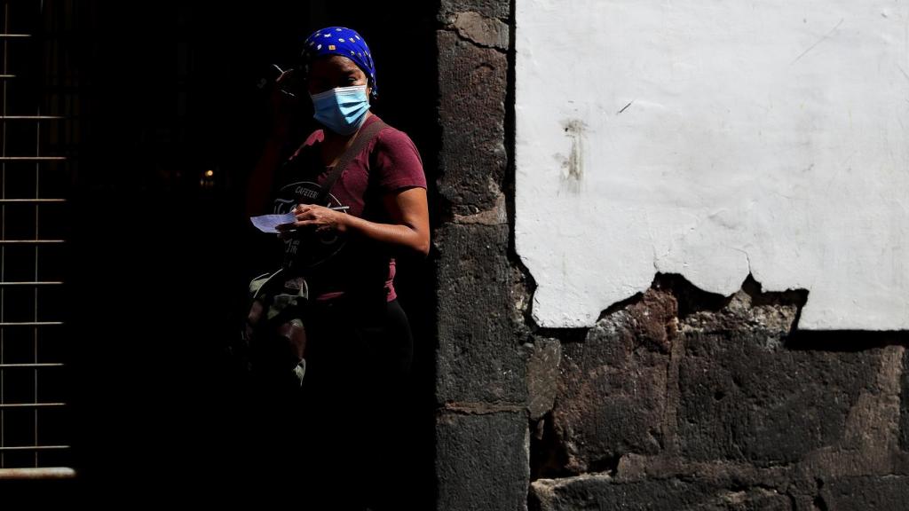 na mujer con mascarilla espera en una calle hoy, en la ciudad de Quito (Ecuador).