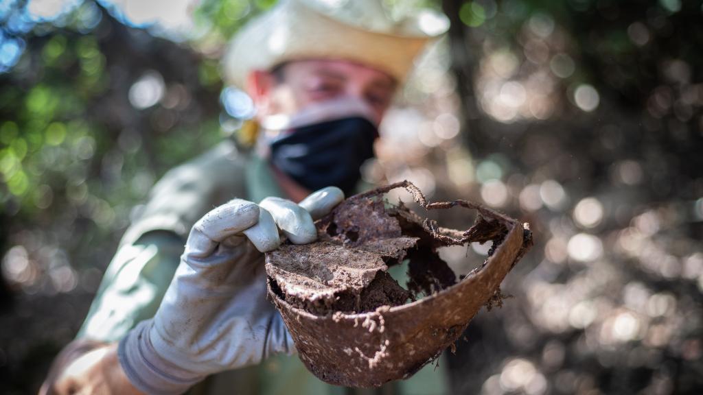 MacGyver recoge e inspecciona una pieza de hierro en el monte.