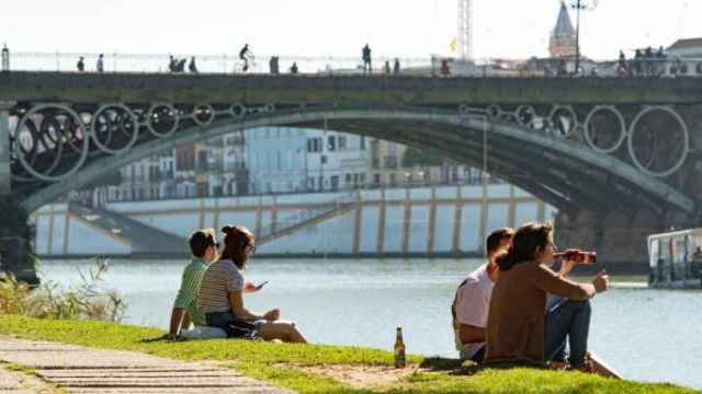 Varias personas en la orilla del Guadalquivir junto al Puente de Triana de Sevilla.
