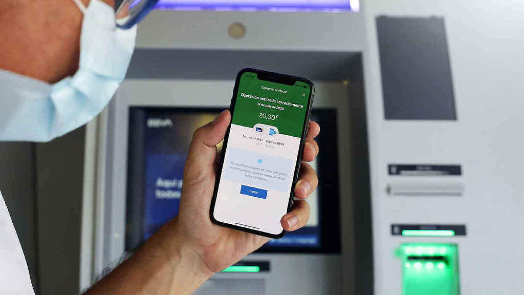Un usuario ante un cajero automático usa una app móvil financiera.