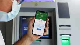 Un usuario ante un cajero automático usa una app móvil financiera.