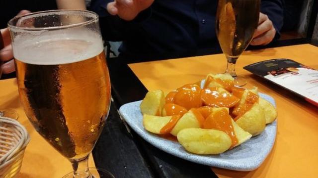 Unas patatas bravas con una caña.