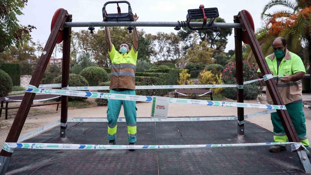 Varios operarios precintan unos columpios en un parque de Valencia este viernes.