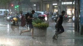 Dos hombres corren por el Paseo de Gracia de Barcelona en mitad de un aguacero.