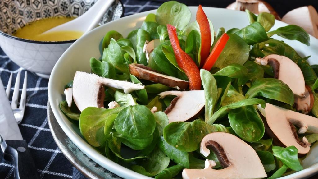 Un plato de ensalada con rúcula y champiñones.