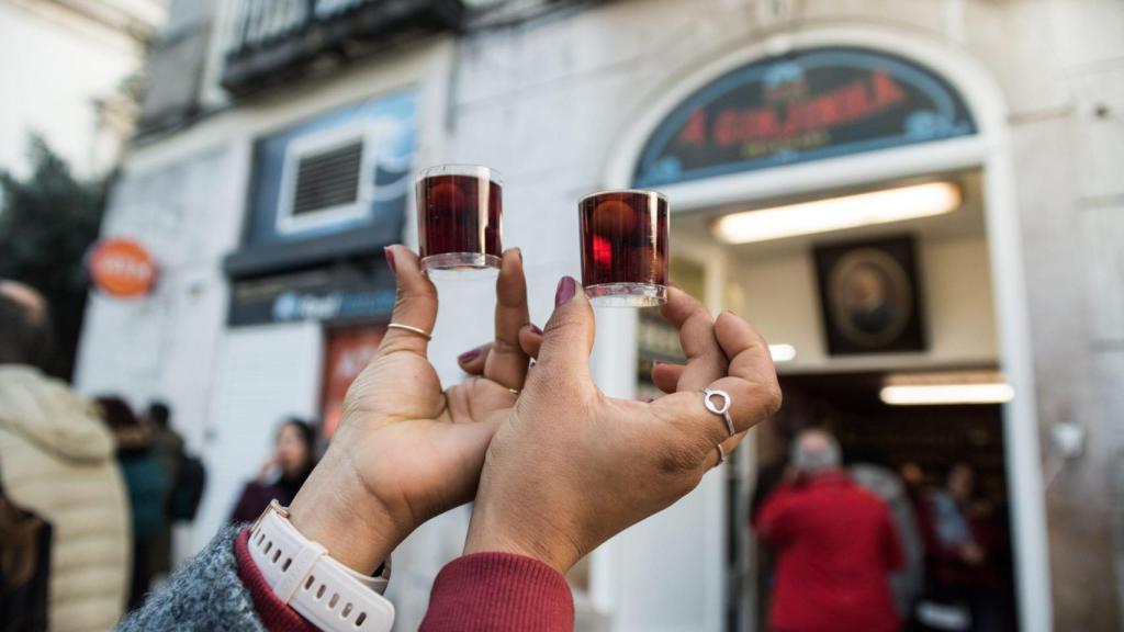 Dos personas sostienen chupitos de Ginjinha frente a un local en Lisboa.