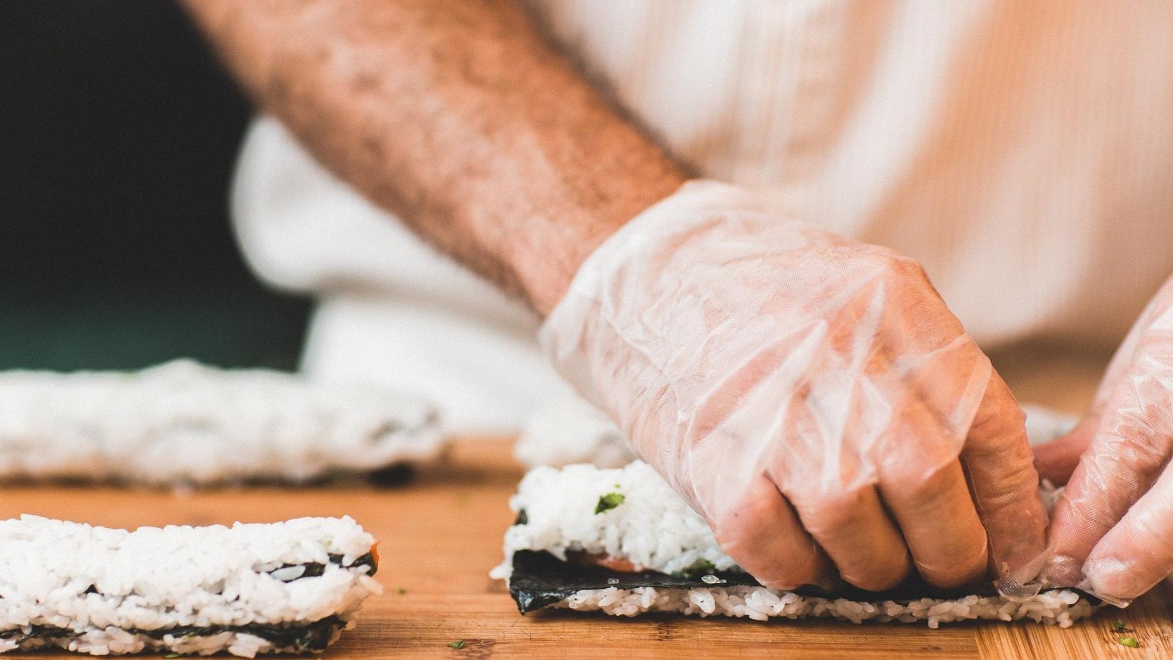 Un hombre cocina sushi con unos guantes.