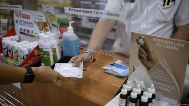 Un farmacéutico entrega a un cliente una de las mascarillas KN95 que ha recibido en su farmacia.