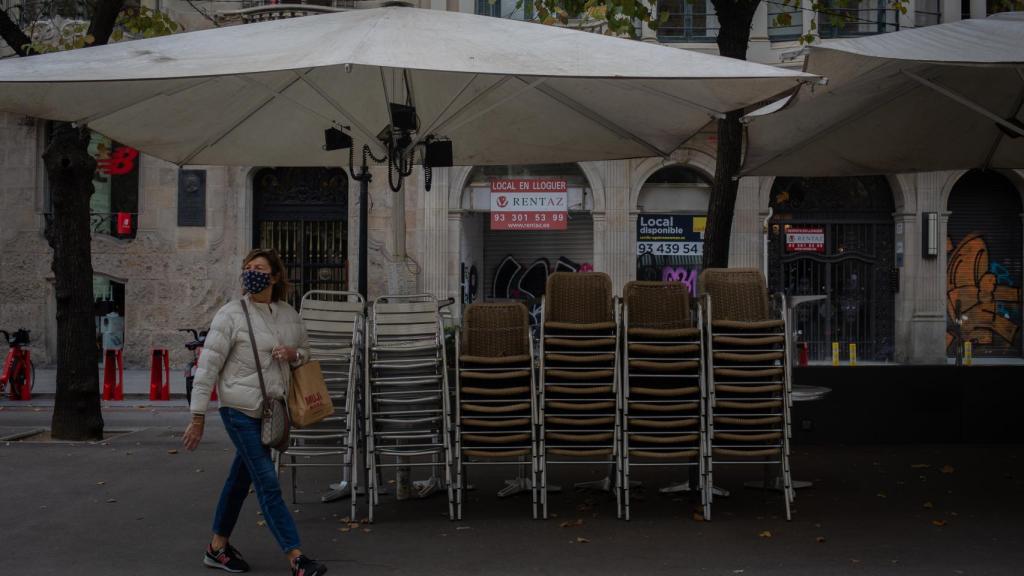 Una mujer pasa junto a la terraza recogida de un bar.