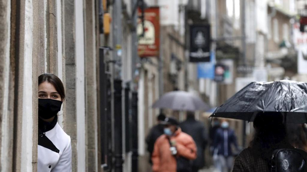 Una empleada de un local en una calle turística observa a los turistas en Santiago de Compostela.