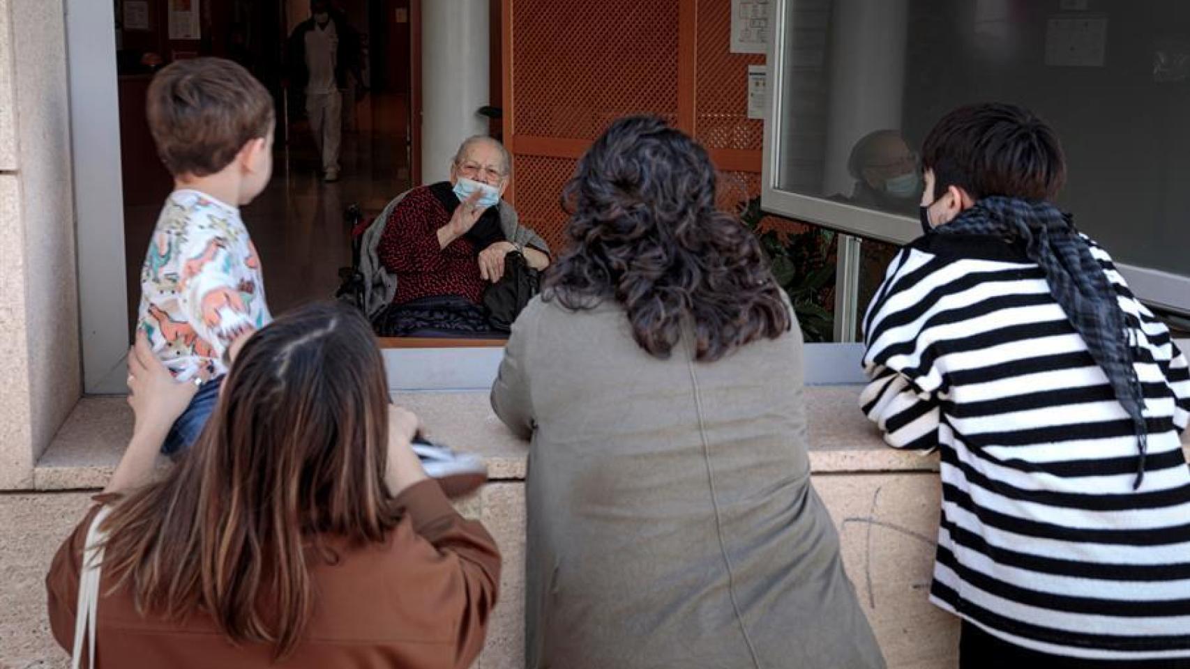 Una anciana recibe la visita de sus nietas a través de una ventana de la residencia de Velluters de Valencia.