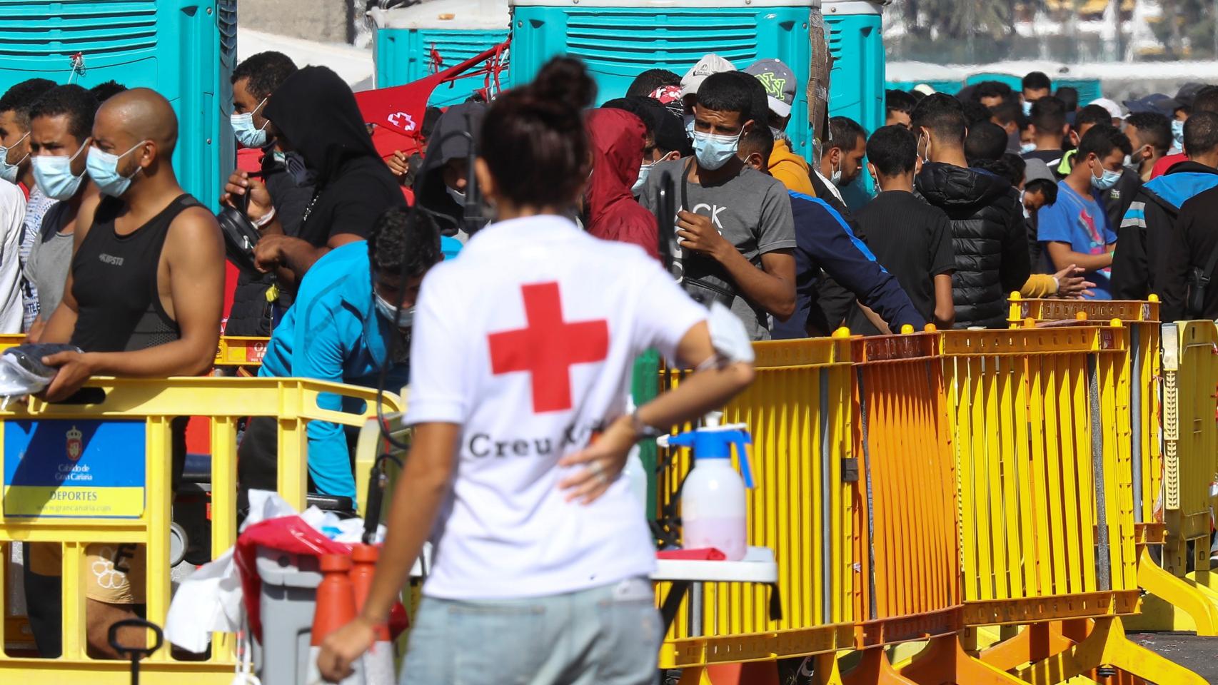Una voluntaria de la Cruz Roja, junto a decenas de inmigrantes en el muelle de Arguineguín.