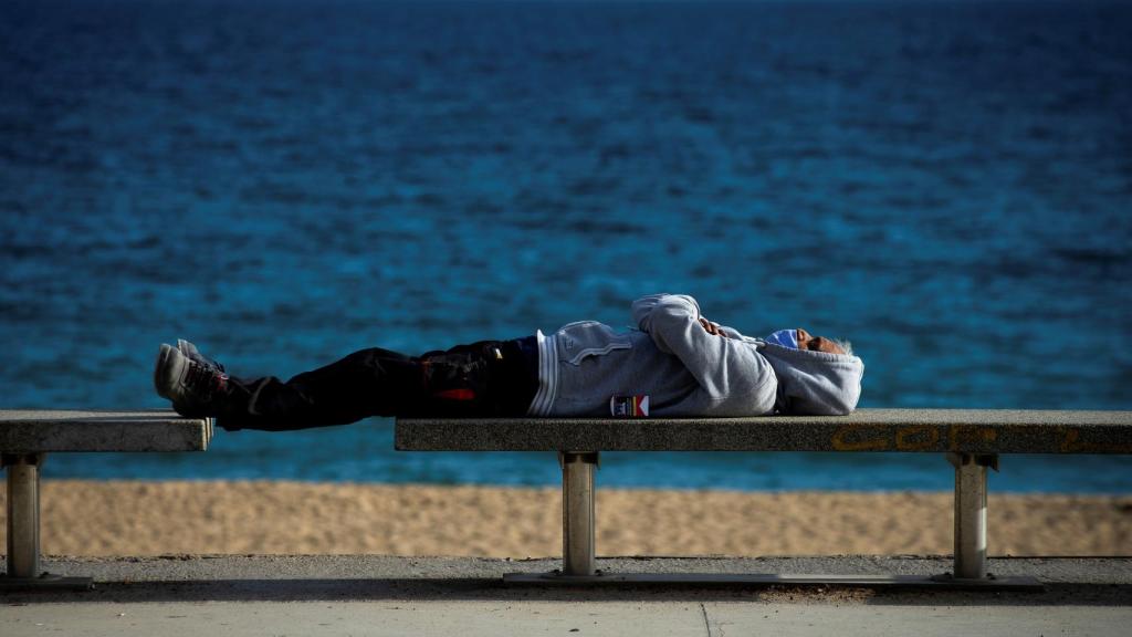 Un hombre con mascarilla descansa en una playa de Barcelona.