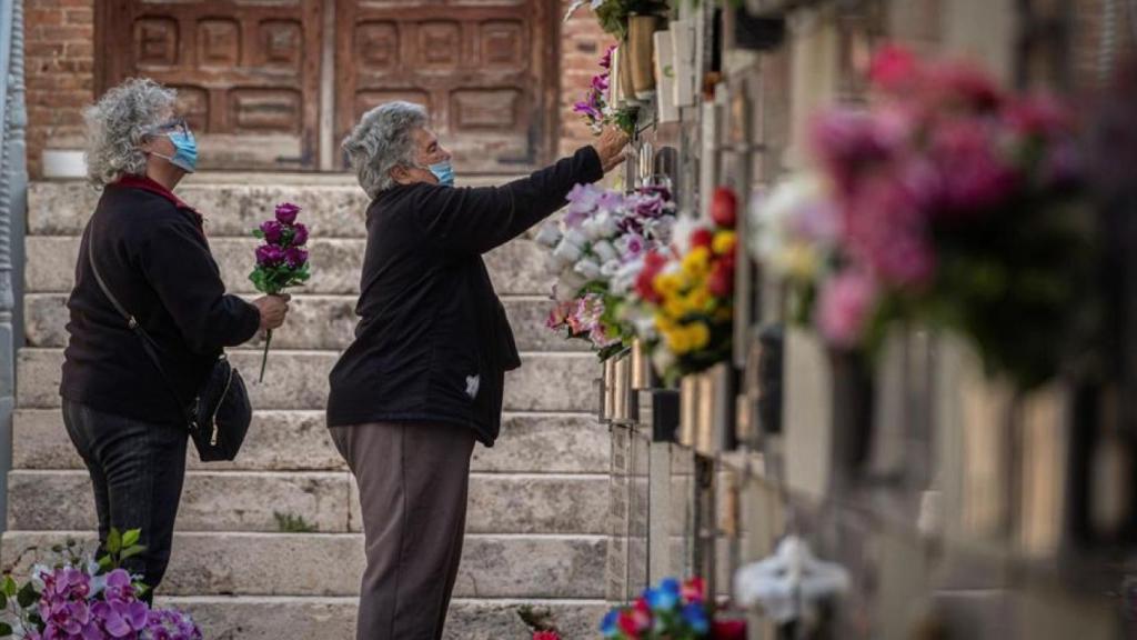 Varias mujeres colocan flores en una tumba del cementerio de Alcalá.