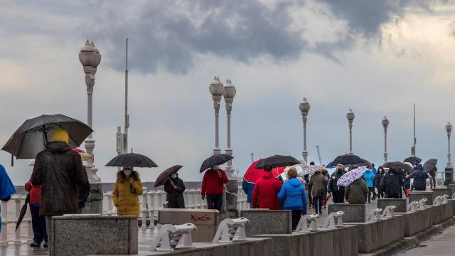 Paseantes bajo la lluvia  junto a la playa de San Lorenzo, en Gijón. EFE/ Alberto Morante