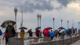 Paseantes bajo la lluvia  junto a la playa de San Lorenzo, en Gijón. EFE/ Alberto Morante