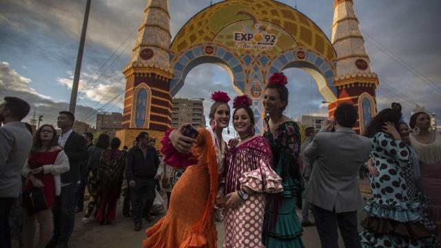 Jóvenes vestidas de flamenca posan ante la portada de la Feria de Abril.