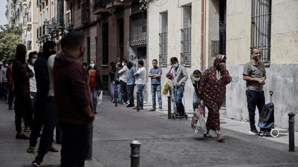 Varias personas hacen cola para recibir alimentos en el barrio madrileño de Lavapies.