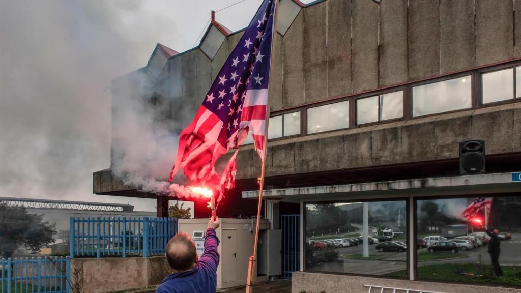 Un trabajador de Alcoa San Cibrao quema una bandera de Estados Unidos delante de la factoría.