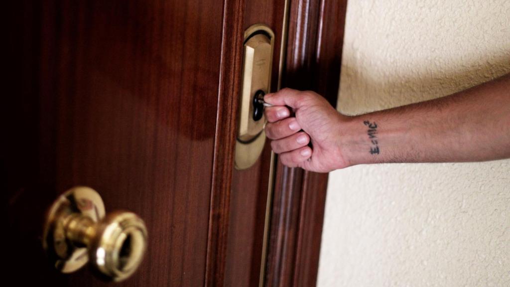 Un hombre introduce una llave en la cerradura de la puerta de una vivienda.