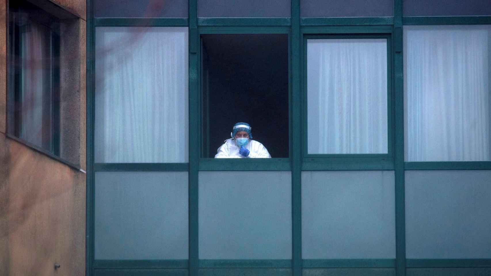 Una trabajadora sanitaria observa desde el interior de una residencia.
