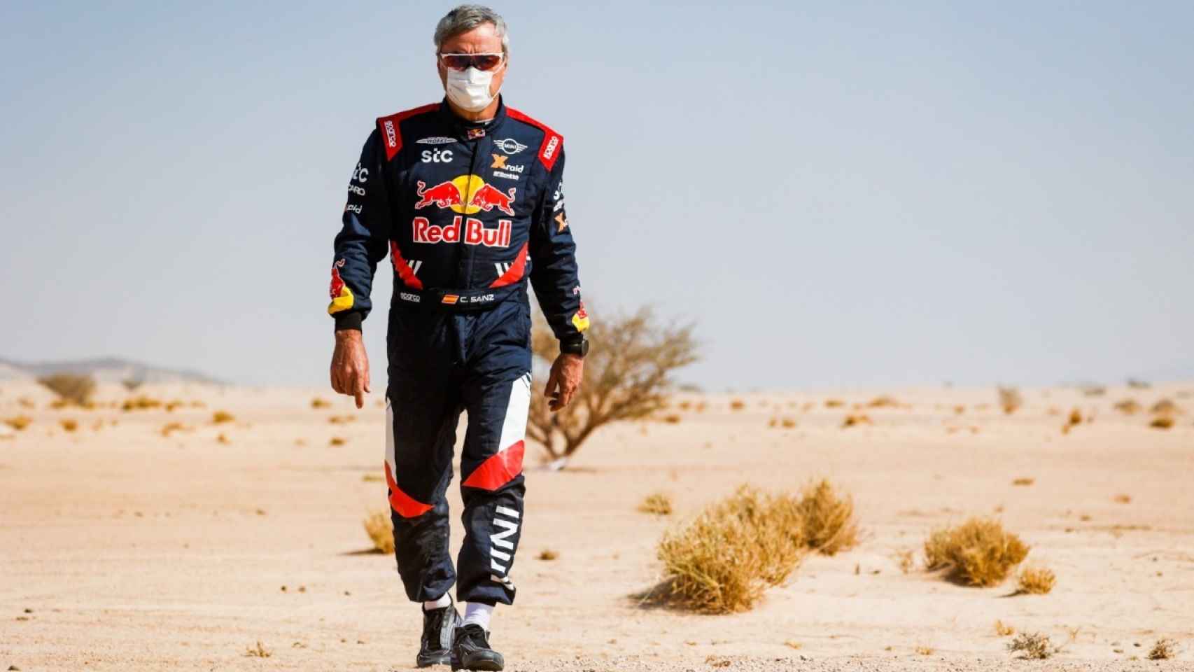 Carlos Sainz camina por la arena del desierto en el Dakar 2021