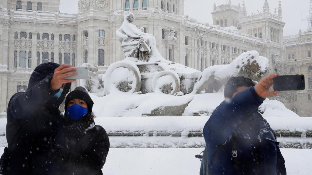 Varias personas se fotografían junto a la Plaza de Cibeles de Madrid.