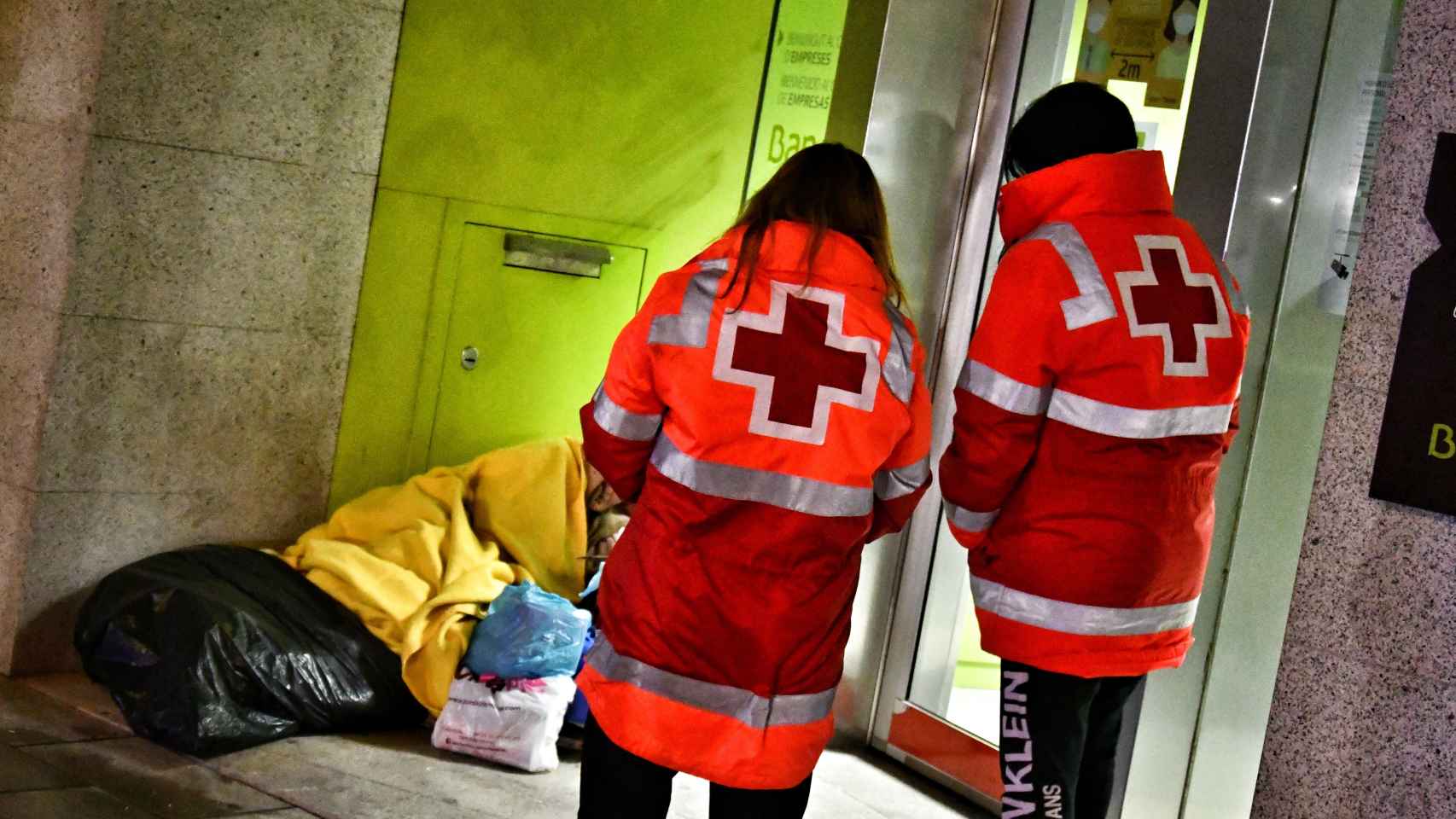 Voluntarios de la Cruz Roja atienden a un hombre que duerme en la calle.