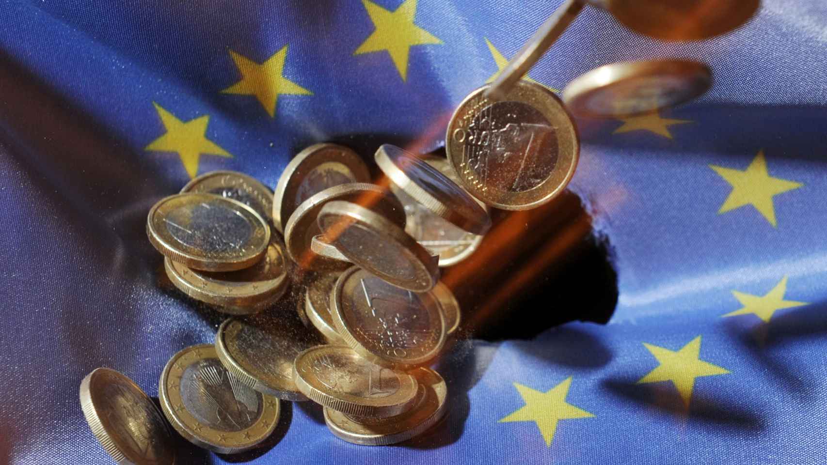Varias monedas de euro sobre una bandera de la Unión Europea.