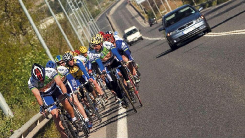 Un coche trata de adelantar un pelotón de ciclistas.