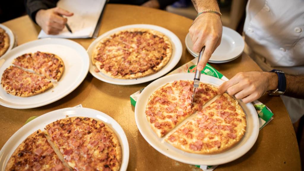 Los hermanos Figurato cortan las pizzas de jamón york y queso.