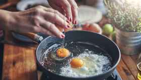 Una mujer fríe huevos en una sartén.